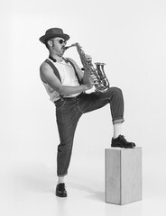 Monochrome. Young stylish man playing saxophone. Live performance. Concept of creativity, retro fashion style, music lifestyle. Black and white portrait