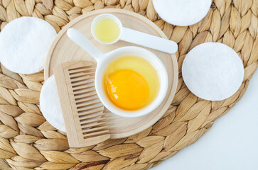 Small bowl with raw egg and wooden hairbrush. Homemade hair or face mask, natural beauty treatment and spa recipe. Top view, copy space. - obrazy, fototapety, plakaty