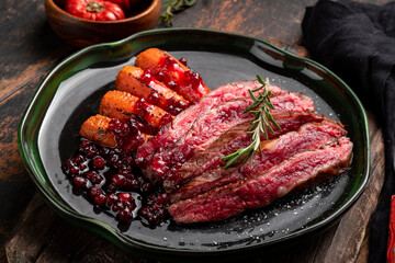 Flank steak fried and chopped with vegetables and cranberry sauce. Beef steak on a plate in rustic style, close up