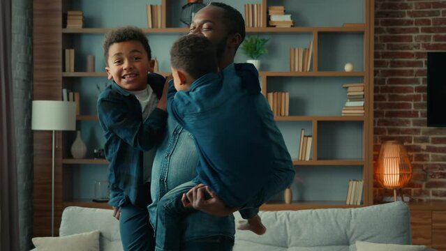 Happy Ethnic Family Playing At Home. African American Father Hold Two Cute Little Children Sons Holding Kids Boys Dancing Together Spinning Around In Living Room Enjoying Funny Weekend In Apartment