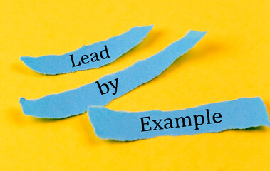 LEAD BY EXAMPLE text on a blue pieces of paper on yellow background, business concept