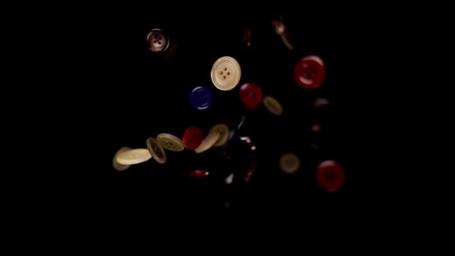 Shining clothes buttons of different colour with electric light reflections fall on black background slow motion macro view