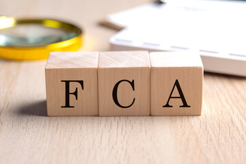 FCA on wooden cubes with magnifier and calculator, financial concept background