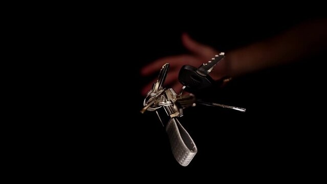 Person hand throws upward keys of black and silver colours with grey keychain and electric light reflections slow motion macro
