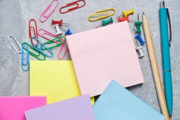 Bundles of multicolored stickers for written notes with chancellery on gray background.