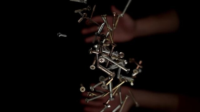 Person hands throw upward various coloured screws and nuts with electric light reflections and catches slow motion macro