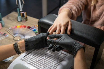 woman beautician filing nails of client with professional electric nail drill in beauty salon. Hardware manicure.