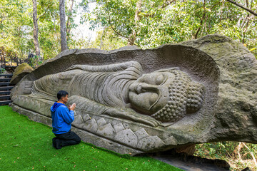 Kalasin, Thailand - February 1, 2023. Buddhist men worship a carved stone Buddha image  at Phu Dan...