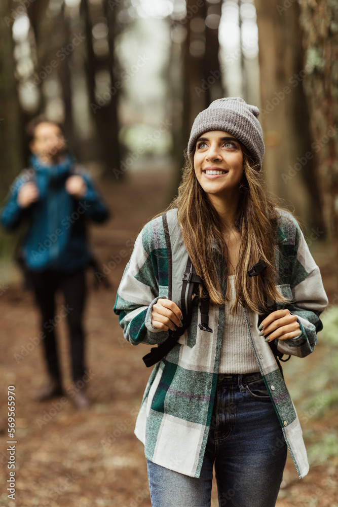 Wall mural smiling inspired young european guy and lady tourists in jackets, hat with backpack walk in autumn f