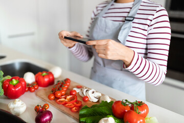 Obraz na płótnie Canvas Unrecognizable woman housewife taking photo of vegetables, kitchen interior