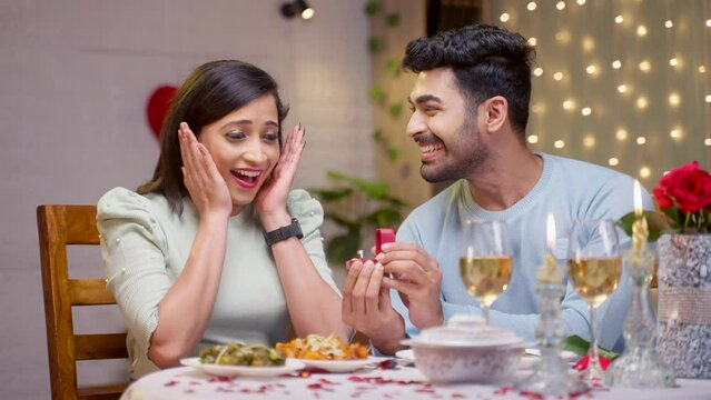 Happy young man proposing to girlfriend offering gold ring durin valentines day at candle light dinner at home - concept of asking a marriage, affection and gift or present.