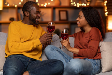 Cheery black couple in casual drinking red wine at home