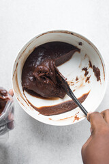 Thick chocolate madeleine batter that has rested in a white bowl, thick chocolate cake batter, brownie batter on a silicone spatula	