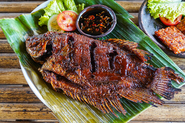 Grilled gurami or grilled gurame with red barbecue sauce, vegetables and chili sauce served on banana leaves,