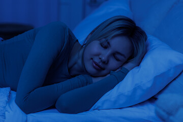 Sleeping young woman lying on pillow in bed at night