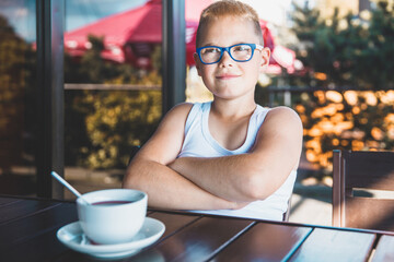 a blond man in glasses sits in a cafe with his arms crossed