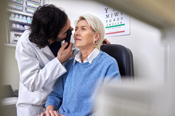 Senior patient in a vision test or eye exam for eyesight by doctor, optometrist or ophthalmologist with medical aid. Mature woman or client with a helpful optician to see retina or check glaucoma