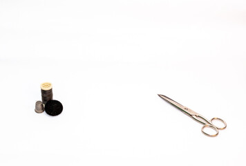 Tijera junto a un rollo de hilo negro con un dedal y un botón negro sobre un fondo blanco.