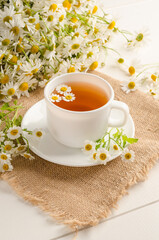 Obraz na płótnie Canvas Healthy chamomile tea in a white cup on a white wooden background with a bouquet of daisies