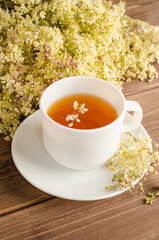Healthy herbal tea with meadowsweet in a white cup on a brown wooden background with a bouquet of meadowsweet