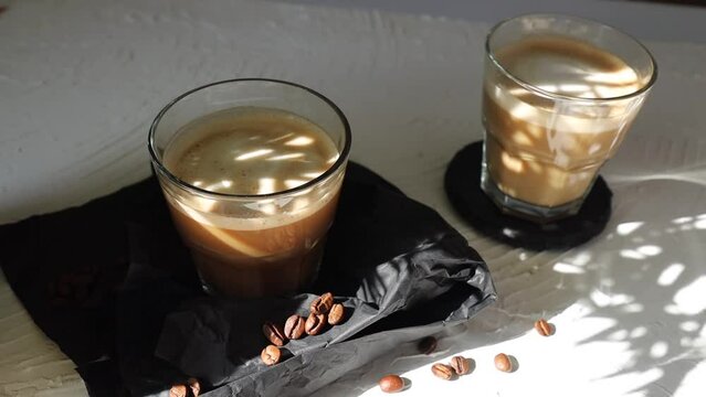 cortado coffee in a glass glass on a stone table with coffee beans. Spanish coffee. hard shadow of the sun from plants
