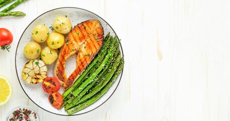 Plate of grilled trout steak, asparagus and potatoes on the white wooden table. Top view, copy space