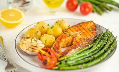 Plate of grilled trout steak, asparagus and potatoes on the table with ingredients.
