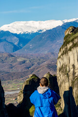 Naklejka premium Scenery sunny day panoramic view, the cliffs of Meteora, Greece with a blurred defocused male figure with blue raincoat
