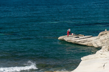 Fishermen are fishing on the seashore. Coast of white stones.