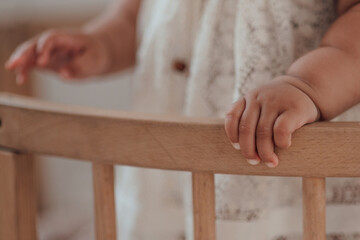 Mixed race toddler girl hands close up in round wooden baby crib at childrens room neutral tones