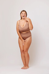 Obraz premium Full lengths shot of positive surprisedEuropean brunette woman in her 30s covers wide opened mouth in shock can not believe her own eyes wears beige underwear. Body positive concept 