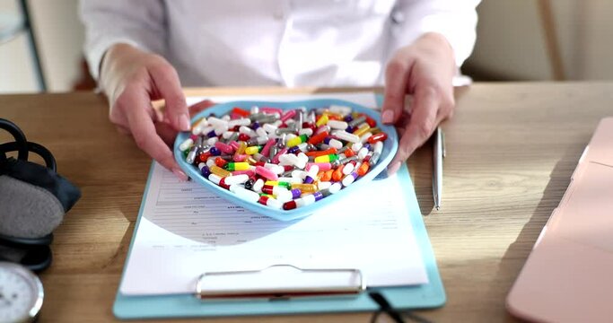 Doctor cardiologist therapist holds a heart plate and many of pills and drugs in hands