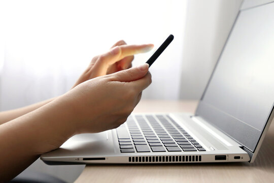 Female hands with smartphone on laptop keyboard background. Woman with mobile phone sitting near the window, concept of online communication, office or home work and payment