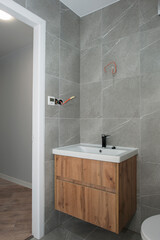 Large bright new bathroom in light colors with gray warm tiled floor, white door against unfinished room.