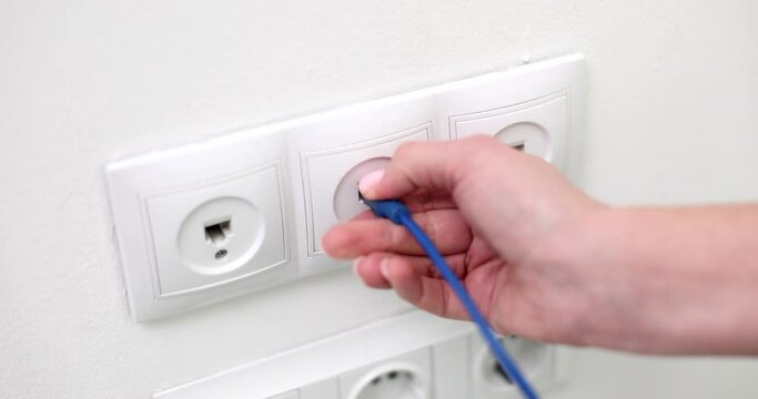 Closeup of woman hand takes out network cable from wall socket