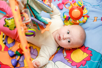 A surprised child lies on a developing mat and looks at the toys with surprise. Bright toy for...