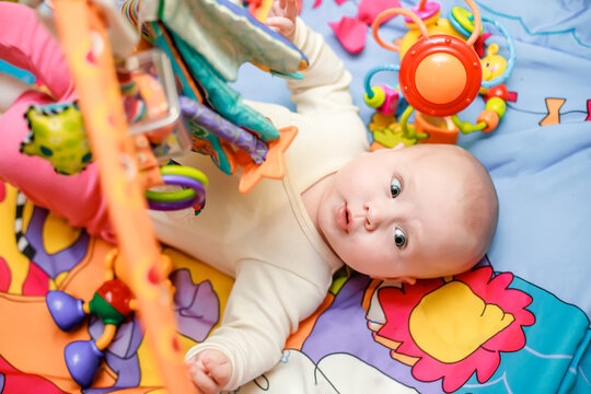 A surprised child lies on a developing mat and looks at the toys with surprise. Bright toy for babies