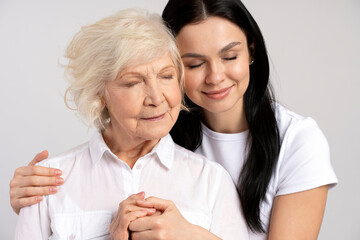 Happy brunette woman hugging with her lovely senior mother isolated on white wall background. Family relationships concept