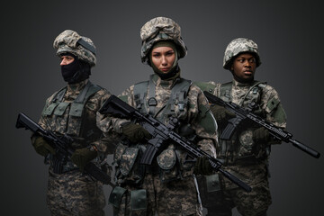 Brave female soldiers with two comrades looking at camera isolated on grey.