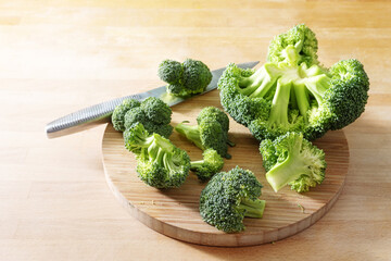 Pieces of raw broccoli and a kitchen knife on a wooden cutting board, healthy vegetable, preparation for cooking a vegetarian meal, copy space, selected focus