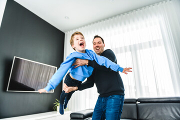 Dad with his cute little boy on a modern house having fun doing air plane on the living room