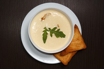 Cream cheese soup with croutons, white bowl, dark wooden background