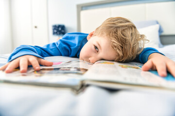 Little boy lying on bed reading book at home