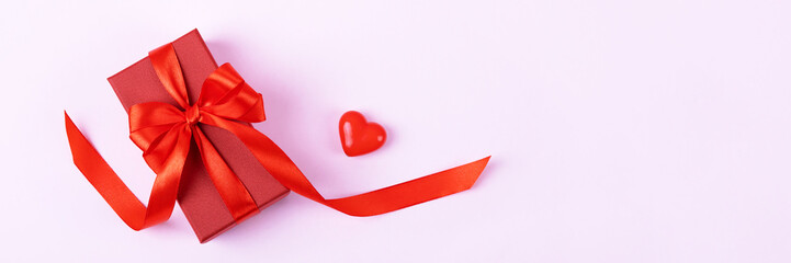 A red gift box with a satin ribbon bow and a decorative heart. Festive banner happy Valentine's Day