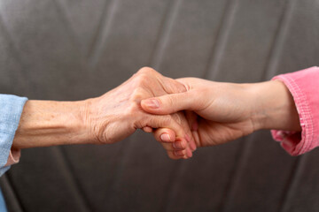 Cropped view of the hands of old woman and her daughter at the sofa background. Family relationships concept