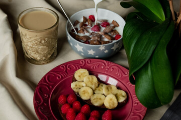 breakfast, cereal with milk, coffee with milk in a faceted glass, beterbrots with chocolate butter, berries and bananas