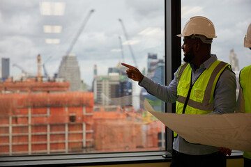 African engineer looking and pointing to building construction site in the office
