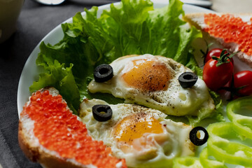 Breakfast, scrambled eggs on lettuce leaves, next to fresh vegetables and a sandwich with red caviar