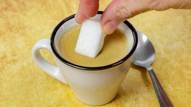  personne mettant du sucre dans un caf&eacute; et le m&eacute;langeant avec une cuill&egrave;re