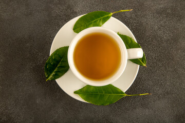 A glass cup of green tea, tea leaves and lemons, on black background
